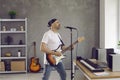 Cool adult man who sings song into microphone and plays electric guitar in his home music studio. Royalty Free Stock Photo