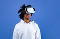 Cool African American guy wearing VR headset, using virtual reality for entertainment on blue studio background Royalty Free Stock Photo