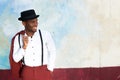 Cool african american male fashion model smiling with vintage suit, suspenders and hat by wall Royalty Free Stock Photo