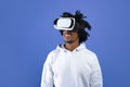 Cool African American teen guy wearing VR headset, using virtual reality for entertainment on blue studio background Royalty Free Stock Photo