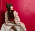 Cool asian kid girl in furcoat and wide pants is posing with her legs wide apart and hands on her knees looking aside Royalty Free Stock Photo