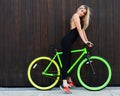 Cool athletic blond girl in black outfit posing with green bright fixed bicycle