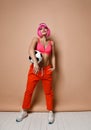 Cool athletic woman with pink hair and stylish visor in bright sportswear is posing with soccer ball under her arm