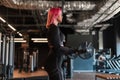 Cool athletic young health girl in a slender body and pink hair in black sportswear does exercise and works out in the hall, side