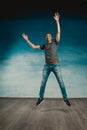 Cool bald man in a gray T-shirt and jeans jumping and fooling around legs wide apart on a blue background, pointing his finger at