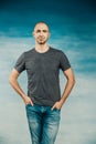 Cool bald man in a gray T-shirt posing holds his hands in his pockets against the background of a blue wall Royalty Free Stock Photo