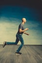 A cool bald man in jeans and a gray T-shirt runs against the background of the greenish wall