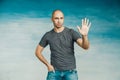 A cool bald man looks at the camera and shows open palm and five fingers,