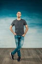 Cool bald man posing in a gray T-shirt holding his hands in his pockets against