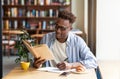 Cool black guy reading book and taking notes during his studies at cafe