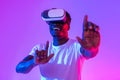 Cool black guy in VR glasses exploring cyberspace, touching imaginary screen, playing virtual reality game in neon light