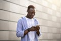 Cool black guy in earphones picking music playlist on mobile phone near brick wall on city street