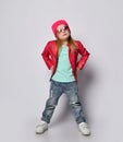 Cool blond baby girl kid in red leather jacket, white t-shirt and blue jeans, sunglasses and hat poses Royalty Free Stock Photo
