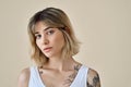 Cool blonde gen z girl pretty face and tattoos at beige background. Portrait.