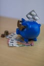 cool blue piggy bank with golden glasses with pills and euro coins and note isolated on wooden table