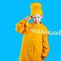 Cool boy in a bright yellow jacket and hat holds a banana in his hands like a phone. On blue background Royalty Free Stock Photo