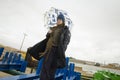 Cool boy in a coat and hat with a scarf posing plays and walks through pipes with an umbrella in an industrial area Royalty Free Stock Photo