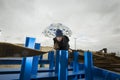 Cool boy in a coat and hat with a scarf posing plays and walks through pipes with an umbrella in an industrial area Royalty Free Stock Photo