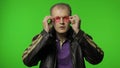 Cool brutal rocker man in brown denim jacket puts on pink sunglasses, looks at camera and smiles Royalty Free Stock Photo