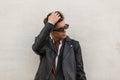 Cool brutal young man in vintage sunglasses in a fashion oversized black leather jacket in a shirt straightens a stylish hairstyle Royalty Free Stock Photo