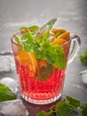 Cool cherry drink with orange and mint in a glass mug with ice cubes on a gray background. Filmed by a large clan