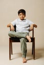 Cool confident indian boy sitting on an armchair in a room over beige background