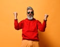 Cool elderly man with a gray beard winner millionaire won raised his hands joyfully in red sweatshirt hoodie shouting