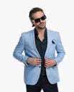 cool fashion guy with sunglasses looking away while buttoning suit Royalty Free Stock Photo