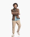 cool fashion model with curly hair in beige jacket crossing arms and walking Royalty Free Stock Photo