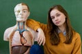 Cool female high school student portrait with an artificial human body model. Student having fun in Biology class.