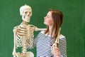 Cool female high school student portrait with an artificial human body skeleton. Student having fun in Biology class.