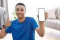 Cool fitness app. Happy arab guy training at home and showing blank smartphone screen at camera, mockup, selective focus