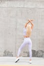 Cool fitness model woman with a beautiful slender figure in fashionable sports clothes and sneakers walks near a gray concrete