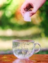 Cool fresh water and ice cube in hand above the transparent glass cup in the table outoors in summer day Royalty Free Stock Photo