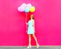Cool girl with an air colorful balloons walking over a pink