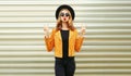 Cool girl blowing red lips sending sweet air kiss wearing yellow jacket, black round hat on wall Royalty Free Stock Photo