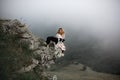 Cool Girl hug dog border collie on edge of rock in fog in mountain smiling Royalty Free Stock Photo