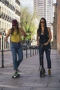 Cool girls couple riding scooter and skate, modern friendship concept