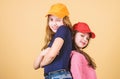 Cool girls. Sisters stand back to back beige background. Little cute girls wearing bright baseball caps. Modern fashion