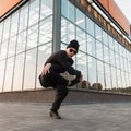 Cool handsome young hipster man dancer in knitted hat in stylish black clothes in trendy sunglasses dancing break dance Royalty Free Stock Photo