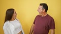 Cool hispanic father and his lovely daughter sharing a surprise, looking amazed over isolated yellow background, showcasing family