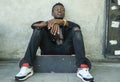 Cool isolated portrait of young attractive and confident hipster black afro American man leaning on street wall holding skate