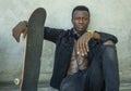 Cool isolated portrait of young attractive and confident hipster black afro American man leaning on street wall holding skate