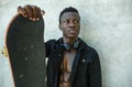 Cool isolated young attractive and confident hipster black African American man leaning on street wall holding skate board as