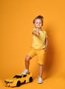 Young boy kid in yellow t-shirt and shorts stepping on a big race car is aiming a finger-gun at us Royalty Free Stock Photo