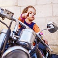 Cool little biker girl playing and having fun on fashioned motorcycle. Humorous portrait of child points to the road with finger Royalty Free Stock Photo