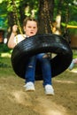 Cool little girl swinging on car rubber wheel with crossed arms in playground in green park. Summer holidays in camp Royalty Free Stock Photo