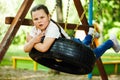 Cool little girl swinging on rubber wheel in playground in green park closeup. Summer holidays in camp, tourist center Royalty Free Stock Photo