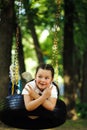 Cool little girl swinging on rubber wheel in playground in green park closeup. Summer holidays in camp, tourist center Royalty Free Stock Photo