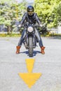 Cool looking motorcycle rider on custom made scrambler style cafe racer on the road with an arrow sign Royalty Free Stock Photo